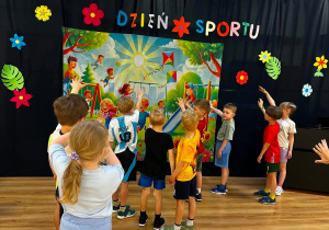 Grupa dzieci wskazuje na plakat związany z Dniem Sportu.
