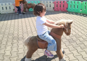 Dziewczynka jedzie na zabawkowym pluszowym koniu.