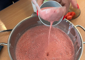 Pani nalewa wazówką koktajl truskawkowy do szklanki.