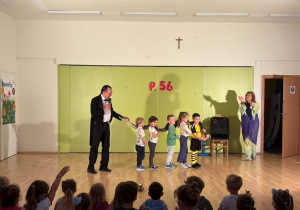 Przedszkolaki wraz z artystami cyrkowymi trzymają węża podczas pokazu.