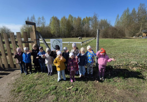 Dzieci z grup Smerfy i Biedronki stoją razem na farmie podczas wycieczki. Uśmiechają się i pozują do wspólnego zdjęcia na świeżym powietrzu.
